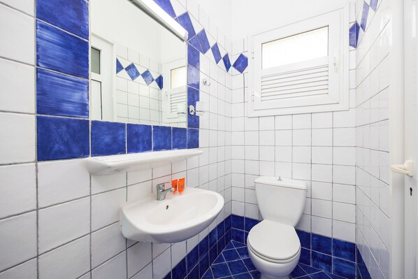 A bathroom with a white sink, blue-tiled floor, and a white toilet. - Koulouris Beach Hotel (Kavos)