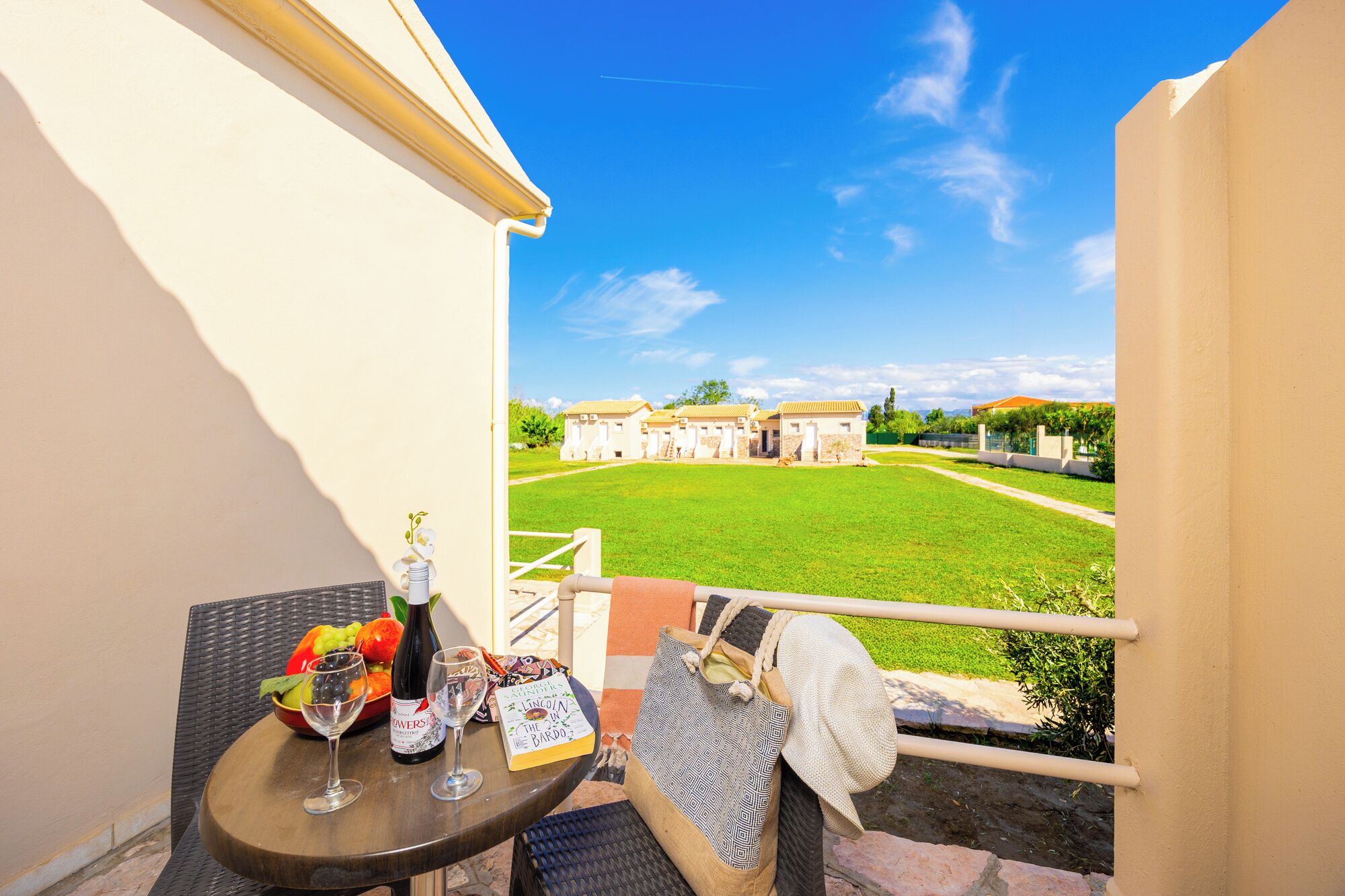 A balcony with a table set for a meal, a view of a courtyard with buildings, and a clear sky.