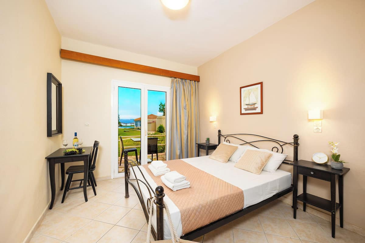 A bedroom with a bed, bedside tables, a desk with a chair, a window with curtains, and a view of the outside.