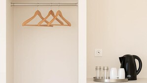 A minimalist room with a white wardrobe, a black kettle, and a small refrigerator.