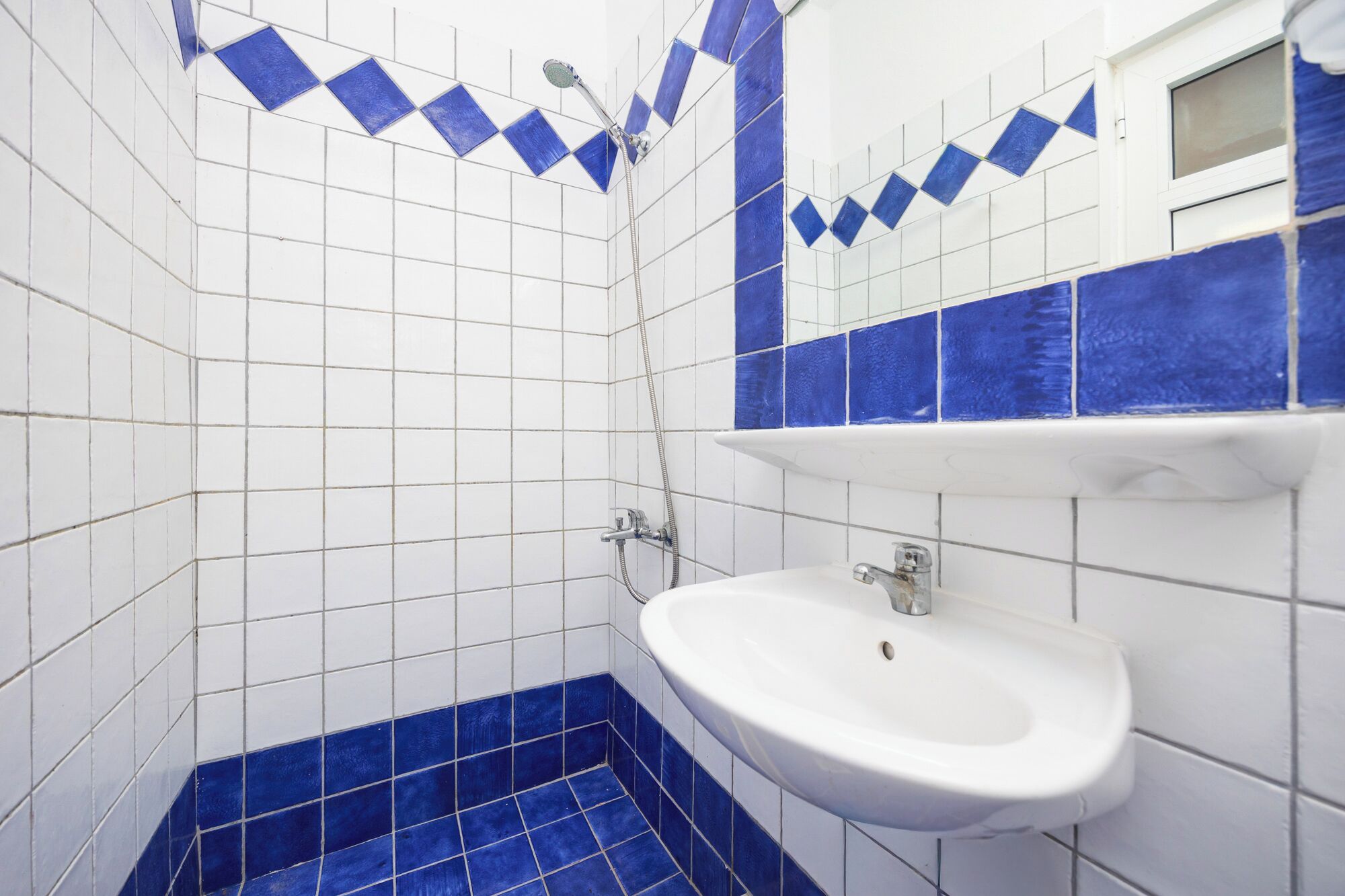 Un bagno con piastrelle bianche e blu, un lavandino bianco e una doccia con soffione manuale.