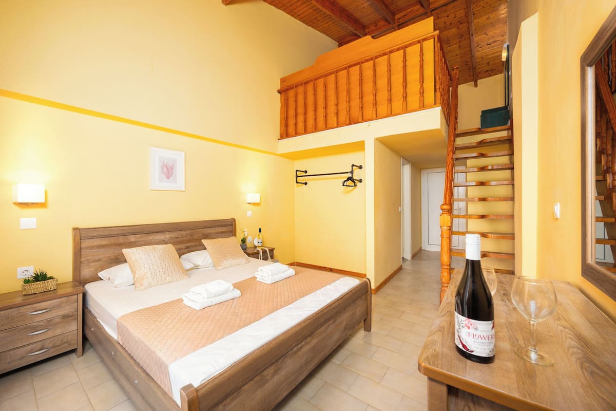 A bedroom with a wooden bed, a nightstand, a wall-mounted towel rack, a bottle of wine, and a wooden staircase.
