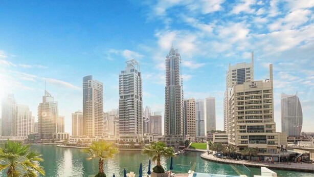 A cityscape with modern high-rise buildings, a marina with boats, and palm trees. - LUX Contemporary Suite with Full Marina View 3 (Dubai)
