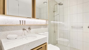 A modern bathroom with a marble sink, a toilet, and a glass-enclosed shower. - Brand-New 2-Bed with Rooftop Access (Northcote)