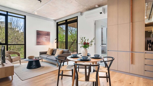 A modern living room with a sofa, a dining table with bowls, and a TV. - Brand-New 2-Bed with Rooftop Access (Northcote)