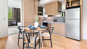 A modern kitchen with wooden cabinets, a stainless steel refrigerator, and a dining area with a round table and chairs. - Brand-New 2-Bed with Rooftop Access (Northcote)