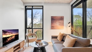 A modern living room with a television, a sofa, a chair, and a coffee table. - Brand-New 2-Bed with Rooftop Access (Northcote)