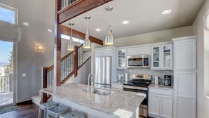 A modern kitchen with granite countertops, stainless steel appliances, and a central island with bar stools. - Stunning Views from a Unique Mountain Cabin! (Jefferson)