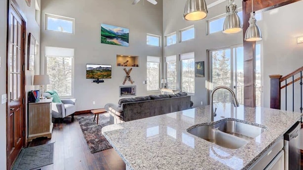 A spacious kitchen with a large island, a dining area with a sofa, and a view of the outdoors through large windows. - Stunning Views from a Unique Mountain Cabin! (Jefferson)