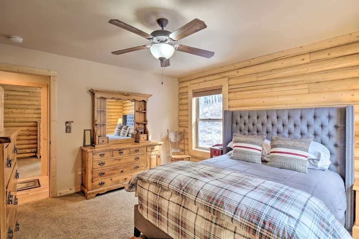 A bedroom with a large bed, a ceiling fan, wooden walls, a dresser, and a mirror.