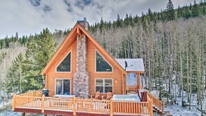 A log cabin with a stone chimney, large windows, and a deck with outdoor seating.