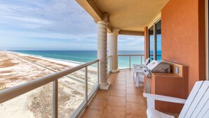 Varanda com vista para a praia e oceano, cadeiras brancas e churrasqueira.