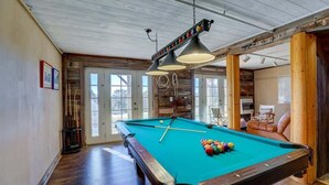 Una mesa de billar en una habitación con vigas de madera y un ventanal grande.