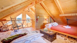 Una cabaña de madera acogedora con un dormitorio en altillo, un pequeño rincón de descanso y un balcón con vistas.