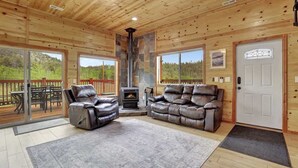 Interior de una cabaña de madera con chimenea, sofás de cuero y una terraza con mobiliario exterior.