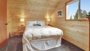 Un dormitorio de cabaña de madera acogedor, con una cama individual, dos lámparas de noche y una ventana con vista a árboles.