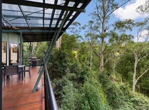 A wooden deck with outdoor furniture, a glass ceiling, and a view of dense forest. - Ecoasis Mami Wata Rainforest Haven (Smiths Creek)