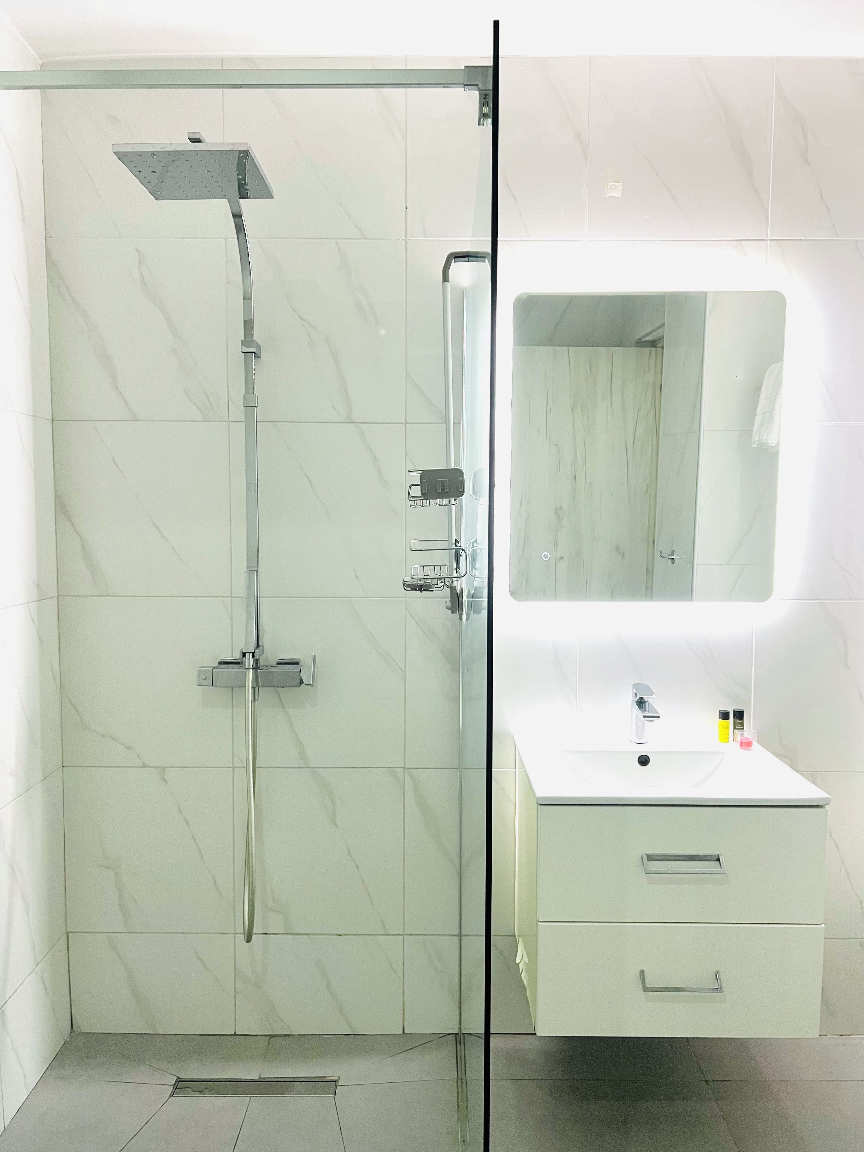 A modern bathroom with a glass-enclosed shower, a white vanity with a mirror, and a tiled floor.