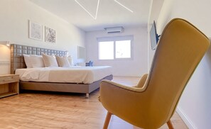 A modern bedroom with a bed, bedside table, chair, and artwork on the wall. - Plateia Suite Deluxe (Nicosia)