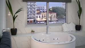 Et moderne badeværelse med et stort badekar, plantepotte og udsigt over byens skyline gennem et stort vindue.