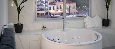 A modern bathroom with a large bathtub, potted plants, and a view of a cityscape through a large window.