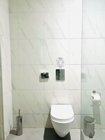 Ett badrum med en toalett, en handtork, en papperskorg och en skylt som uppmanar att man inte ska spola ner pappershanddukar i toaletten.