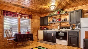 Un interior de madera con una mesa de comedor, sillas, una zona de cocina con electrodomésticos y una alfombra colorida.