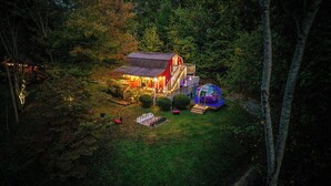 Une maison à l’extérieur rouge, dotée d’une terrasse en bois et surmontée d’une structure en forme de dôme de verre.