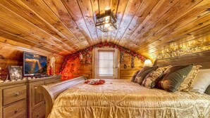 Une chambre chaleureuse, décorée dans un style rustique avec du bois, comprenant un grand lit, une commode et un téléviseur posé sur un meuble en bois.