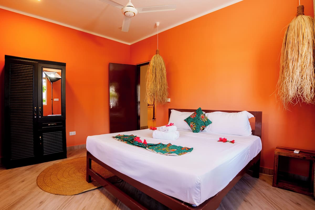 Une chambre d’hôtel avec un mur orange, un lit avec du linge de maison blanc, une tête de lit en bois et une lampe suspendue.
