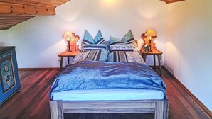 Une chambre avec un plafond en pente, un lit avec de nombreux oreillers, deux tables de chevet avec des lampes et une armoire en bois.