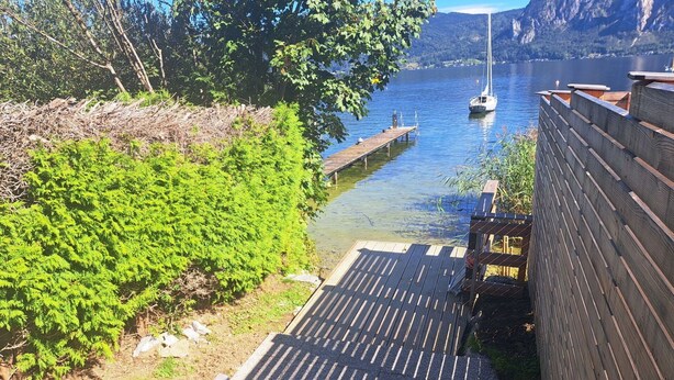 Une terrasse en bois avec un banc, donnant sur un lac paisible où flotte un voilier.