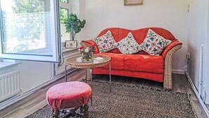 Une pièce chaleureuse avec un canapé rouge, une petite table ronde, un fauteuil en osier et un pouf rouge.