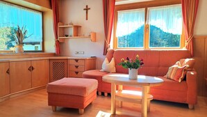 A cozy living room with a wooden floor, a sofa, a small table with a plant, and a cross on the wall. - Wonderful private villa for 9 guests with TV, balcony, pets allowed and panoramic view (Wald Im Pinzgau)