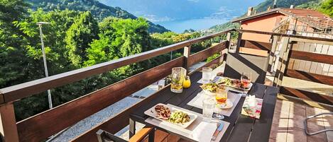 A dining table with food and drinks, a chair, and a view of mountains and a lake.