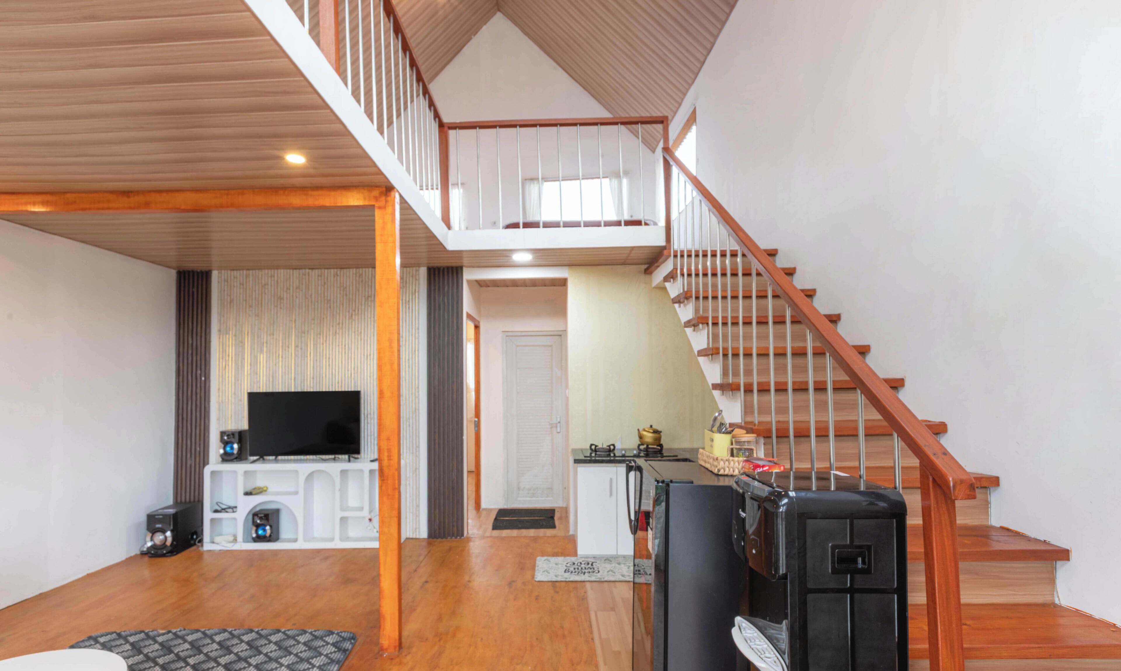 A spacious living area with a wooden staircase, a television, and a kitchen area.