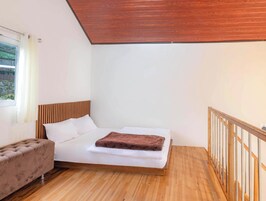 Un dormitorio con cama, cabecera de madera, ventana con cortinas, piso de madera y baranda de madera.