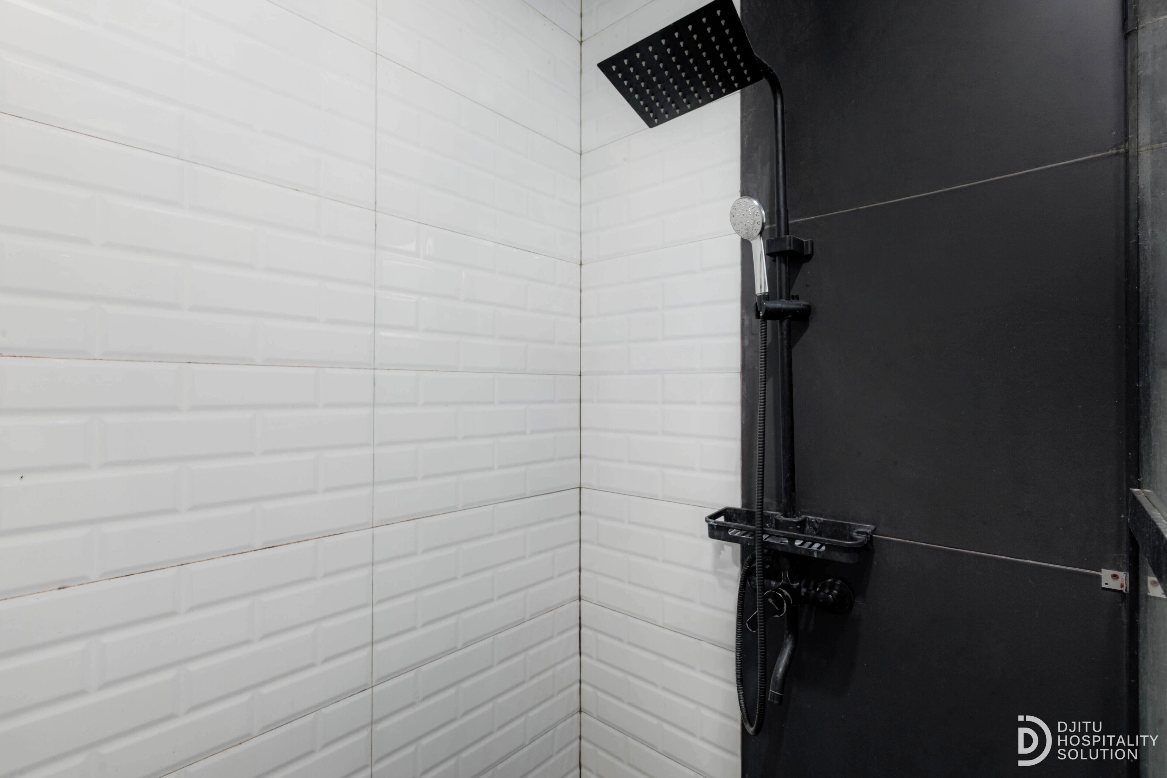 Une salle de bain avec des murs recouverts de carreaux blancs, un receveur de douche noir et une pomme de douche visible.