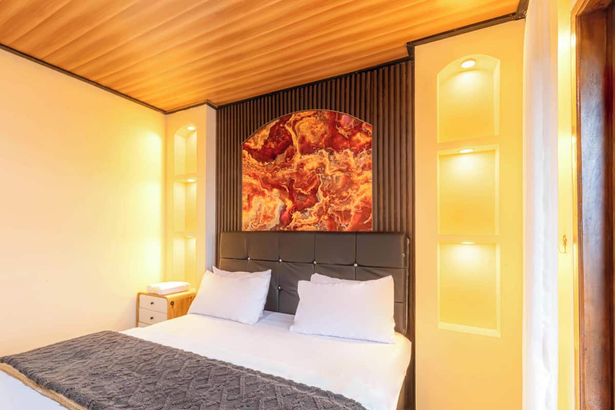 Een hotelkamer met een bed, hoofdeinde, een kunstwerk aan de muur en een nachtkastje.