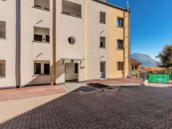 A multi-story building with a central entrance, a courtyard with a drainage grate, and a mountain in the background.