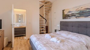 Un dormitorio con cama, un baño con lavabo, una escalera y un cuadro en la pared.