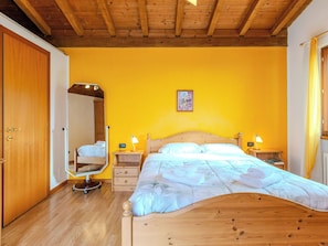 A bedroom with a wooden bed, a mirror, two bedside tables with lamps, and a yellow wall.