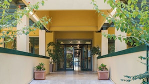 Un ingresso di un edificio con pavimento piastrellato, piante in vaso e una porta in vetro che dà sull'interno.