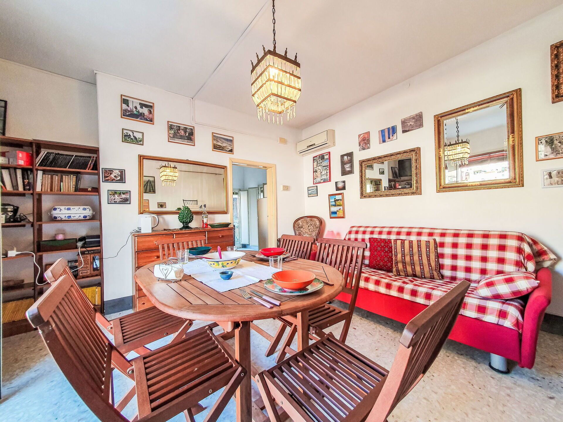 A cozy living room with a dining table, wooden chairs, a red and white checkered sofa, and a chandelier.