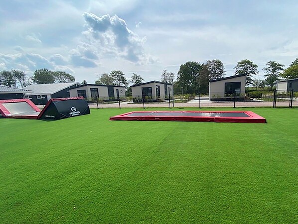 Un espace extérieur doté d’une pelouse artificielle, d’un trampoline rouge et d’une structure de jeu noire et rouge.