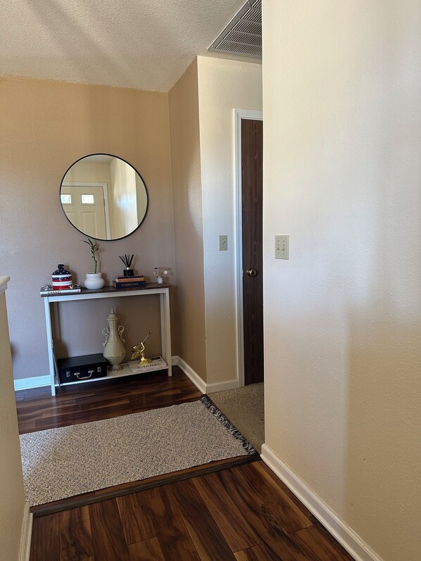 A hallway with a white console table, a mirror, a door, and a wooden floor.