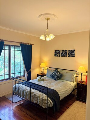 Une chambre à coucher comprenant un lit, deux lampes de chevet, une fenêtre avec des rideaux, un luminaire au plafond et des œuvres d’art murales.