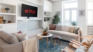 A modern living room with a sofa, coffee table, and a TV mounted on the wall displaying 'NETFLIX'. - Luxury Penthouse | Sauna | Balcony | AirCon (Helsinki)