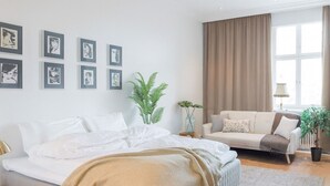 A bedroom with a bed, a sofa, a window with curtains, and framed pictures on the wall. - Luxury Penthouse | Sauna | Balcony | AirCon (Helsinki)