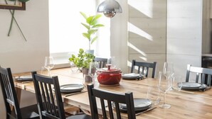 A dining table set with plates, glasses, and a red pot, surrounded by chairs in a room with a large window and a plant. - Luxury Penthouse | Sauna | Balcony | AirCon (Helsinki)